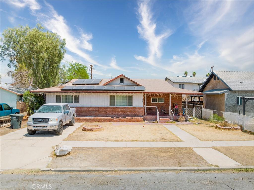 634 W Holt Ave, El Centro, CA 92243 - single story home featuring brick siding, solar panels, covered porch, and driveway