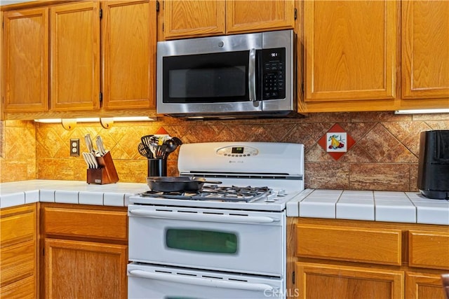 1457 Quiet Ct, Merced, CA 95340 - kitchen featuring stainless steel microwave, white range with gas cooktop, tile countertops, decorative backsplash, and brown cabinets