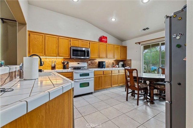 1457 Quiet Ct, Merced, CA 95340 - kitchen with appliances with stainless steel finishes, tile countertops, vaulted ceiling, tasteful backsplash, and light tile patterned flooring