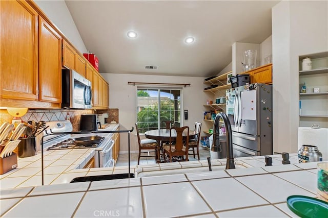 1457 Quiet Ct, Merced, CA 95340 - kitchen with tile counters, appliances with stainless steel finishes, vaulted ceiling, tasteful backsplash, and open shelves