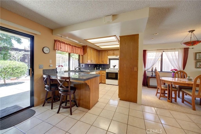 4185 Vanguard Dr, Lompoc, CA 93436 - kitchen with white electric range, a peninsula, a textured ceiling, light tile patterned flooring, and brown cabinets