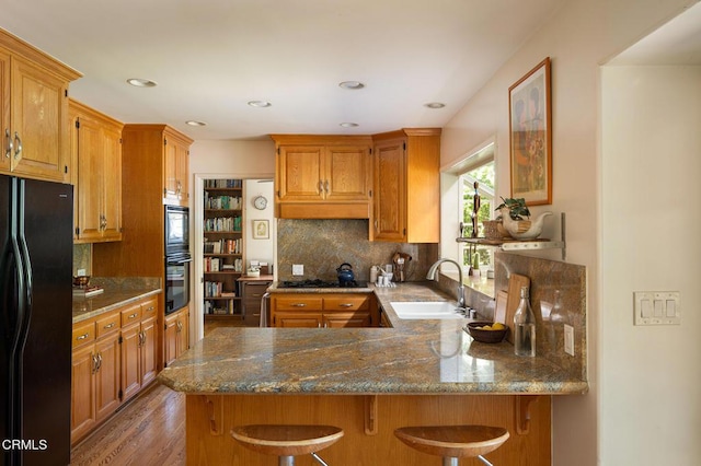 394 S Bonnie Ave, Pasadena, CA 91106 - kitchen with black appliances, a peninsula, tasteful backsplash, light wood-style flooring, and a breakfast bar area