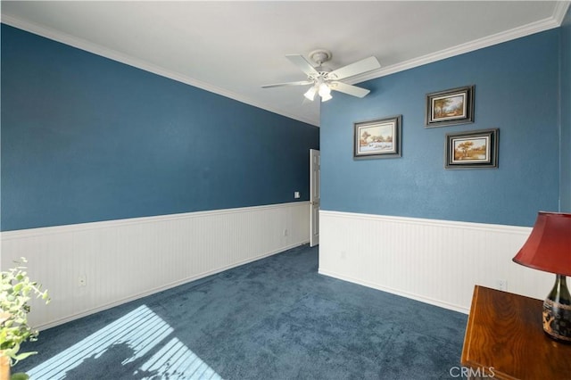 spare room featuring a ceiling fan, wainscoting, ornamental molding, and carpet flooring