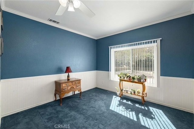 unfurnished room with a wainscoted wall, a ceiling fan, carpet flooring, and ornamental molding