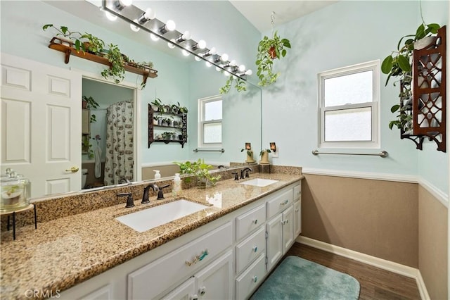 bathroom featuring wood finished floors, double vanity, baseboards, and curtained shower
