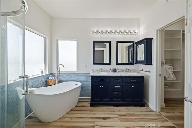 full bathroom featuring double vanity, a soaking tub, wood finished floors, tile walls, and a wainscoted wall