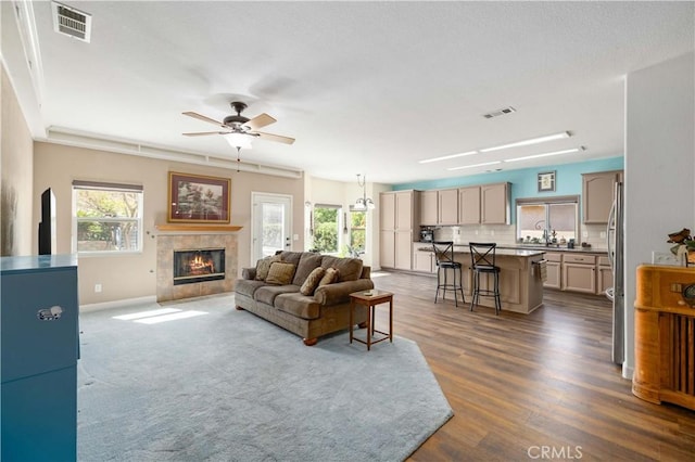 living room featuring ceiling fan, a fireplace, dark wood-style flooring, and baseboards