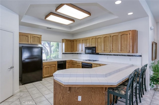 1542 E Alluvial Ave Unit 258, Fresno, CA 93720 - kitchen with black appliances, a raised ceiling, a peninsula, tasteful backsplash, and brown cabinetry