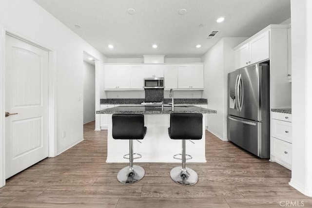 16075 Osprey Ave, Chino, CA 91708 - kitchen with stainless steel appliances, a breakfast bar area, white cabinetry, dark stone countertops, and a sink