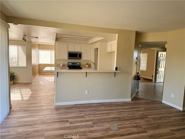 15620 Smoke Tree St, Hesperia, CA 92345 - kitchen featuring stainless steel microwave, range, a peninsula, white cabinets, and wood finished floors