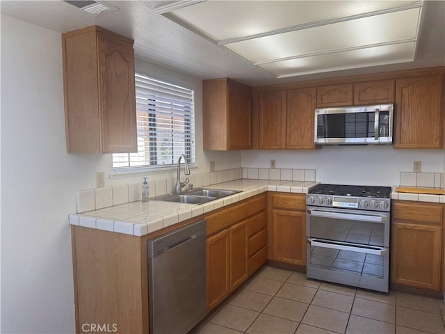 19126 Frances St, Apple Valley, CA 92308 - kitchen featuring appliances with stainless steel finishes, a sink, light tile patterned floors, and brown cabinetry