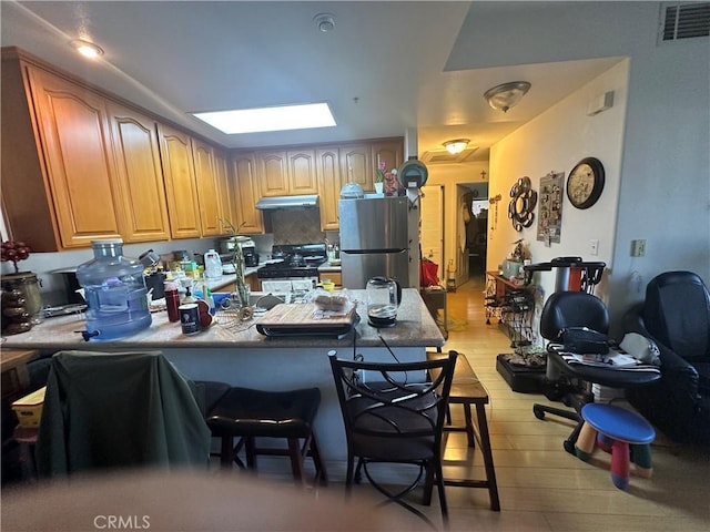 17888 Alburtis Ave Unit B112, Artesia, CA 90701 - kitchen featuring under cabinet range hood, freestanding refrigerator, range with gas stovetop, a peninsula, and a breakfast bar