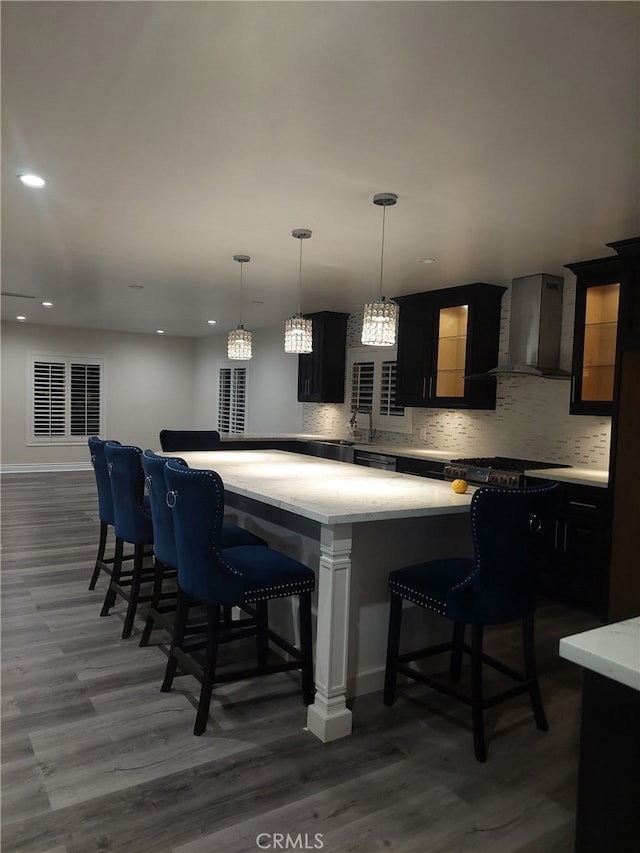 11022 Maple St, Whittier, CA 90601 - kitchen with wall chimney range hood, a kitchen breakfast bar, backsplash, wood finished floors, and recessed lighting