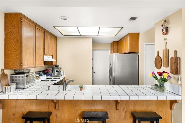 3516 Landsford Way, Carlsbad, CA 92010 - kitchen featuring freestanding refrigerator, electric stove, under cabinet range hood, tile countertops, and brown cabinetry