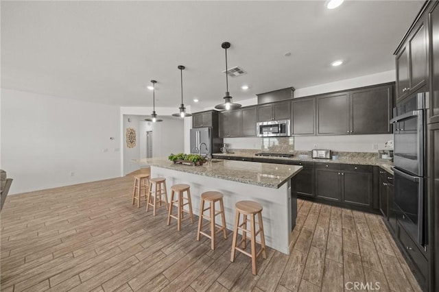 11066 Guffey Ranch Way, Corona, CA 92883 - kitchen with stainless steel appliances, light wood-style flooring, a kitchen island with sink, a kitchen bar, and recessed lighting