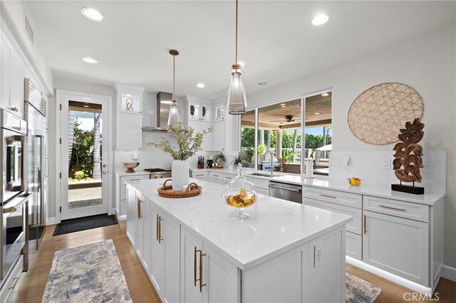 18976 Rockinghorse Ln, Huntington Beach, CA 92648 - kitchen featuring white cabinets, a kitchen island, appliances with stainless steel finishes, decorative light fixtures, and wall chimney exhaust hood