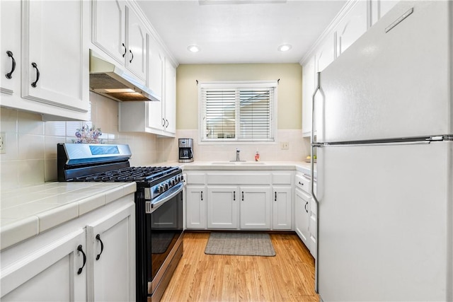 11628 Cedarvale St, Norwalk, CA 90650 - kitchen featuring freestanding refrigerator, stainless steel range with gas cooktop, under cabinet range hood, light wood-type flooring, and white cabinets