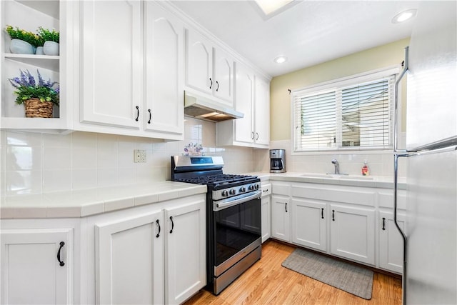 11628 Cedarvale St, Norwalk, CA 90650 - kitchen with stainless steel gas stove, freestanding refrigerator, under cabinet range hood, tile counters, and white cabinetry