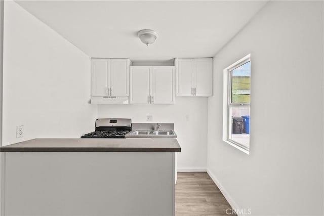 821 W 43rd Pl, Los Angeles, CA 90037 - kitchen featuring gas range, under cabinet range hood, a sink, white cabinets, and baseboards