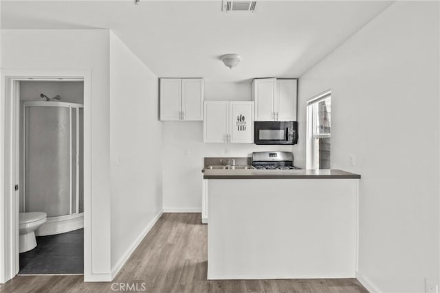 821 W 43rd Pl, Los Angeles, CA 90037 - kitchen featuring black microwave, gas range, white cabinets, wood finished floors, and baseboards