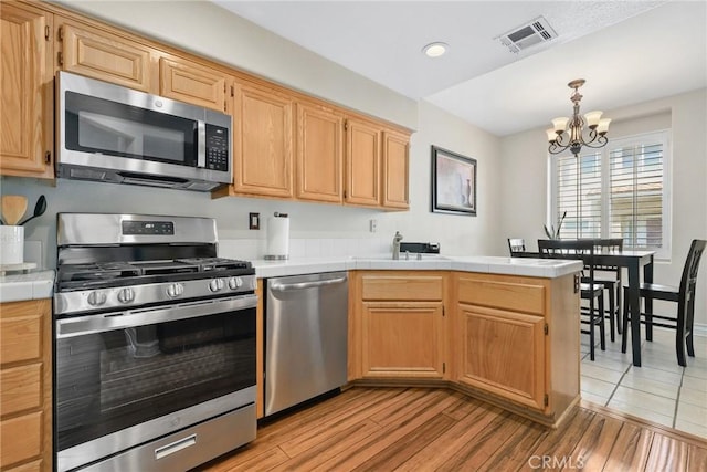 18102 Flynn Dr Unit 4602, Canyon Country, CA 91387 - kitchen with appliances with stainless steel finishes, a chandelier, tile counters, a sink, and light wood-style floors