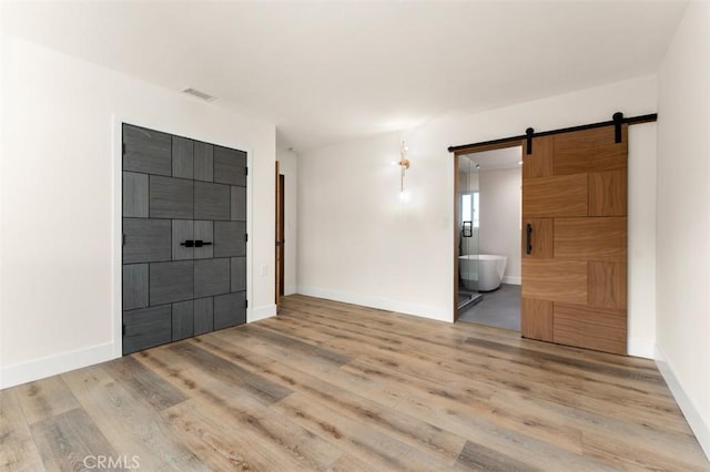 60468 Latham Trl, Joshua Tree, CA 92252 - unfurnished bedroom with a barn door, ensuite bathroom, wood finished floors, and baseboards