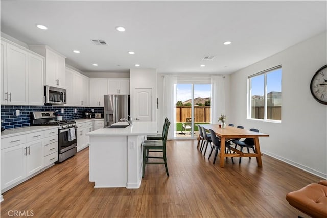 3615 Santa Monica Ct, Rosamond, CA 93560 - kitchen featuring stainless steel appliances, a center island with sink, light countertops, backsplash, and wood finished floors