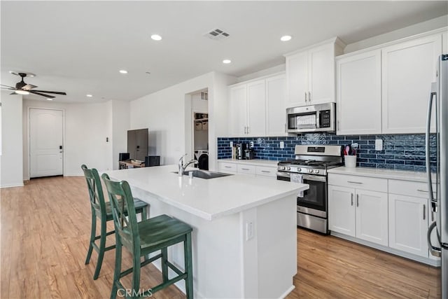 3615 Santa Monica Ct, Rosamond, CA 93560 - kitchen with stainless steel appliances, decorative backsplash, a breakfast bar area, a kitchen island with sink, and light wood-style flooring