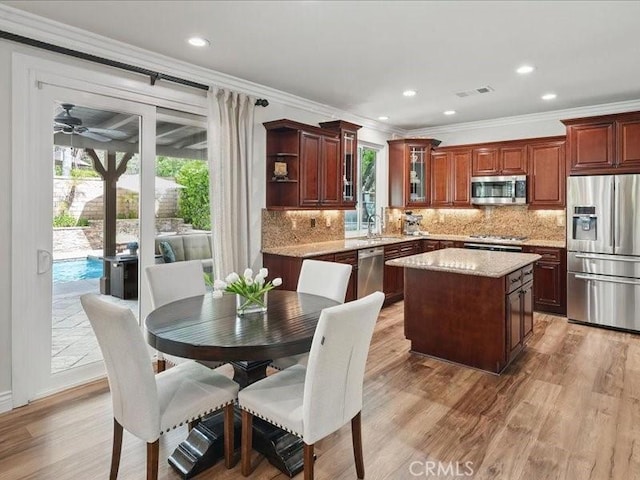 27718 Heartwood Ct, Valencia, CA 91354 - kitchen featuring appliances with stainless steel finishes, crown molding, a center island, light wood finished floors, and decorative backsplash