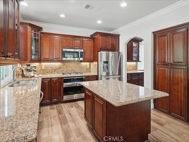 27718 Heartwood Ct, Valencia, CA 91354 - kitchen featuring appliances with stainless steel finishes, a sink, arched walkways, light wood-style flooring, and light stone counters