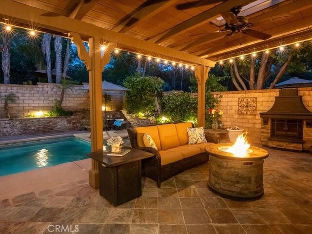 27718 Heartwood Ct, Valencia, CA 91354 - patio at night with a patio area, ceiling fan, a fenced backyard, and an outdoor living space with a fireplace