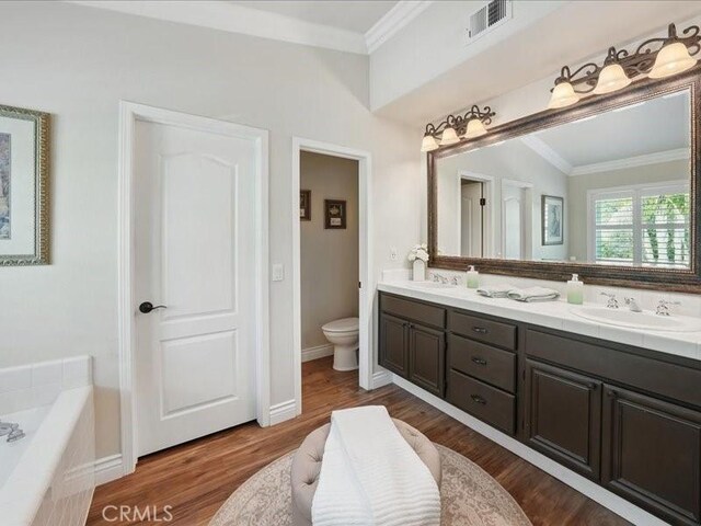 27718 Heartwood Ct, Valencia, CA 91354 - bathroom featuring crown molding, toilet, double vanity, wood finished floors, and a relaxing tiled tub