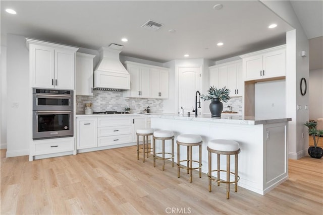 13165 N Bluffs Ct, San Miguel, CA 93451 - kitchen with custom exhaust hood, stainless steel double oven, light wood-style flooring, tasteful backsplash, and recessed lighting