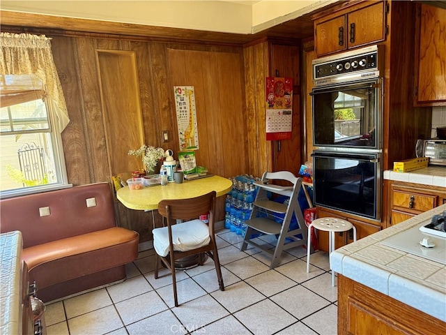 2277 Cogswell Rd, El Monte, CA 91732 - kitchen featuring tile counters, brown cabinets, light tile patterned floors, plenty of natural light, and wooden walls