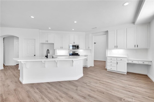 29 Villa Valtelena, Lake Elsinore, CA 92532 - kitchen with appliances with stainless steel finishes, arched walkways, white cabinets, light wood-style floors, and a kitchen island with sink