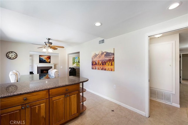 21848 Ute Way, Lake Forest, CA 92630 - kitchen featuring a lit fireplace, baseboards, a ceiling fan, brown cabinetry, and light stone counters