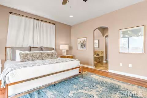 62398 Cope Ln, Joshua Tree, CA 92252 - bedroom featuring baseboards, wood finished floors, arched walkways, ensuite bathroom, and a ceiling fan