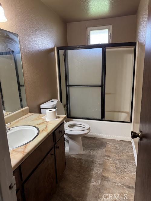 1447 W Westward Ave, Banning, CA 92220 - bathroom with a textured wall, toilet, vanity, combined bath / shower with glass door, and a textured ceiling