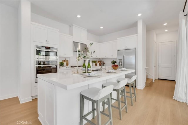 119 Zawn, Irvine, CA 92618 - kitchen featuring appliances with stainless steel finishes, light wood-style floors, white cabinets, a kitchen island with sink, and a kitchen bar