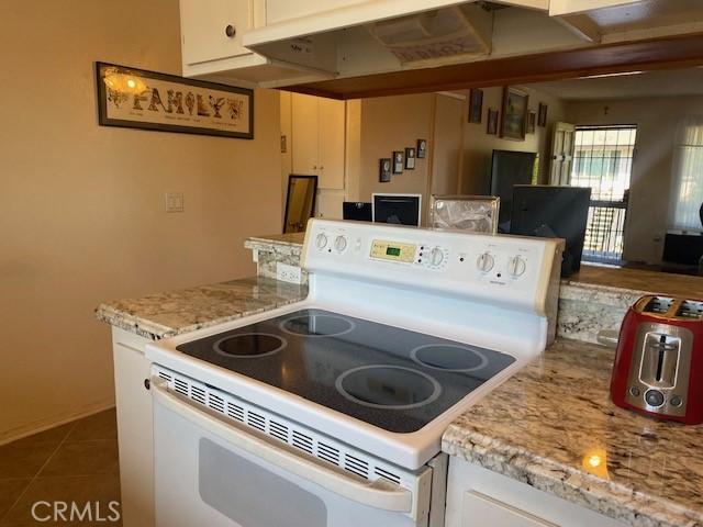7100 Cerritos Ave Unit 112, Stanton, CA 90680 - kitchen featuring white electric range, white cabinets, light stone counters, and dark tile patterned floors