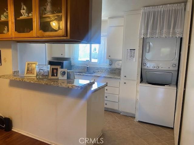 7100 Cerritos Ave Unit 112, Stanton, CA 90680 - kitchen with stacked washer / dryer, light stone countertops, white cabinets, glass insert cabinets, and a sink