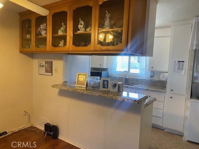 7100 Cerritos Ave Unit 112, Stanton, CA 90680 - kitchen with light stone counters, glass insert cabinets, a peninsula, a sink, and white cabinetry