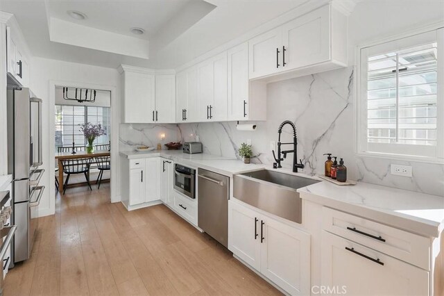 24148 Saint Moritz Dr, Valencia, CA 91355 - kitchen with stainless steel appliances, a sink, backsplash, white cabinetry, and a tray ceiling