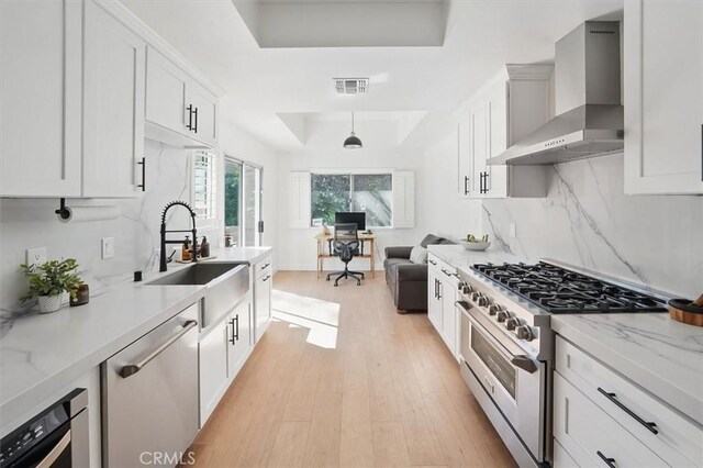 24148 Saint Moritz Dr, Valencia, CA 91355 - kitchen featuring appliances with stainless steel finishes, a tray ceiling, wall chimney exhaust hood, a sink, and light wood-style floors