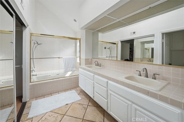 24148 Saint Moritz Dr, Valencia, CA 91355 - bathroom featuring double vanity, backsplash, vaulted ceiling, tiled shower / bath, and stone tile flooring