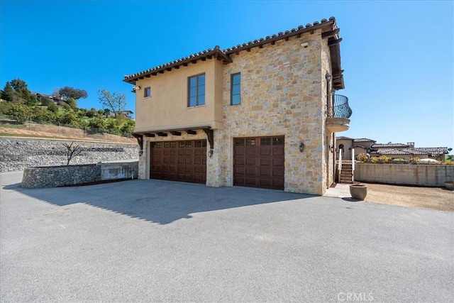 1470 Via Chaparral, Fallbrook, CA 92028 - view of side of property featuring a garage, stone siding, a balcony, asphalt driveway, and stucco siding