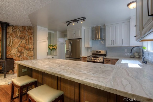 6125 Desabla Ln, Magalia, CA 95954 - kitchen with appliances with stainless steel finishes, wall chimney exhaust hood, a sink, a wood stove, and a peninsula