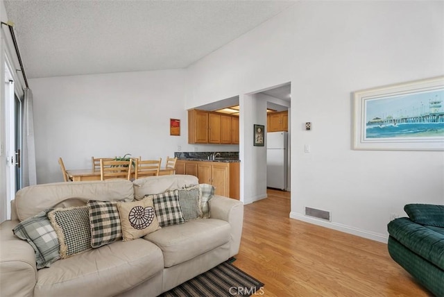 17152 Pacific Coast Unit 19, Huntington Beach, CA 92649 - living area featuring light wood-style floors, baseboards, vaulted ceiling, and a textured ceiling