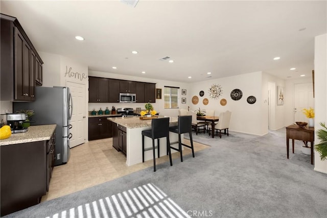4337 Rima Dr, Fontana, CA 92336 - kitchen featuring appliances with stainless steel finishes, a kitchen island, a breakfast bar area, dark brown cabinetry, and recessed lighting