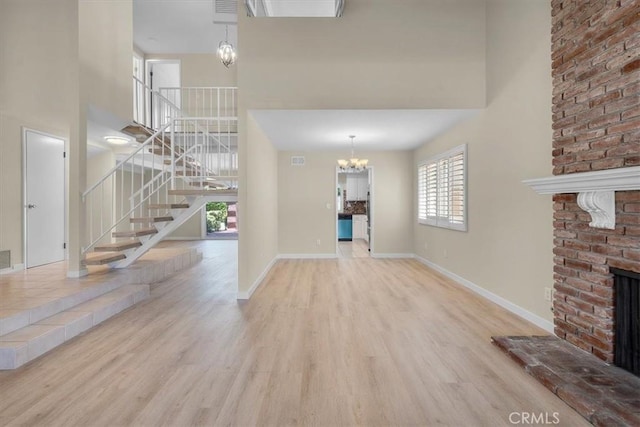 19924 Mildred Ave, Torrance, CA 90503 - unfurnished living room featuring a towering ceiling, stairway, a brick fireplace, a chandelier, and wood finished floors